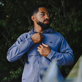 Man adjusting his blue golf jacket with a brand logo against a dark background