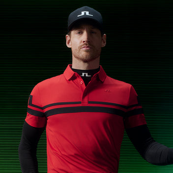 Man wearing a red golf polo shirt with black stripes and a cap on a dark background