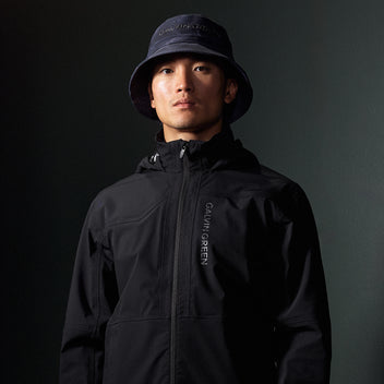 Person wearing a black golf jacket and hat with 'Calvin Klein' branding on a dark background